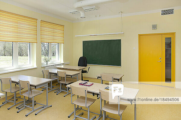 A newly built school classroom with desk and chairs. Windows with yellow blinds.