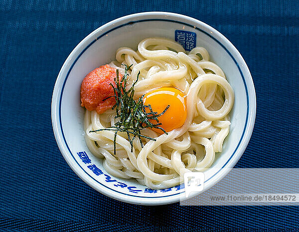 A dish of noodles  vegetables and fish with a yellow egg yolk.