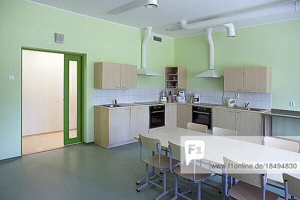 A modern school  a kitchen with fitted cupboards and ovens  a long table and chairs.