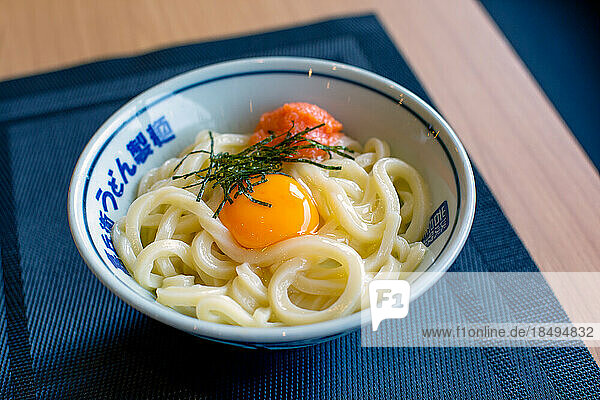 A dish of noodles  vegetables and fish with a yellow egg yolk.