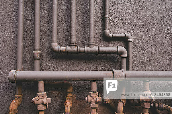 Natural gas utility pipes running along a brown wall  valves and joints.