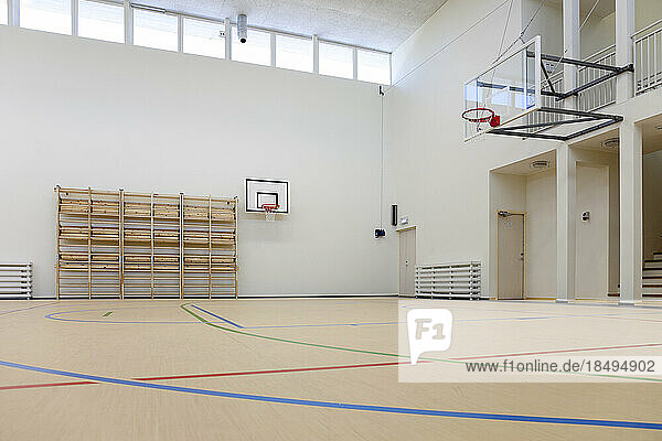 Indoor basketball court at a school. Wooden floor and marked court  a hoop and backboard.