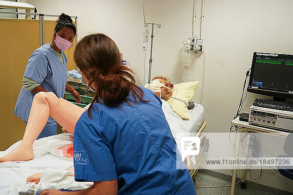 Students facing a post natal emergency follow procedures on a mannequin. This dummy is controlled by operators in an adjoining room. Here  a woman with heavy bleeding following a home birth.
