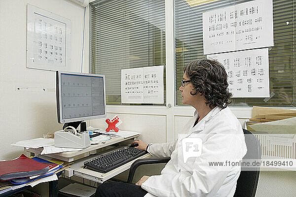 Cytogenetics laboratory  surrounded by karyotypes  a doctor analyzes the results of a sample in order to write a report.