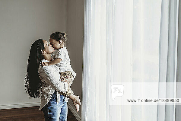 Young mother with long hair holding toddler boy and kissing in studio