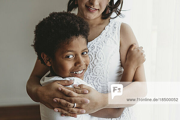 Close up portrait of smiling son being hugged by mother
