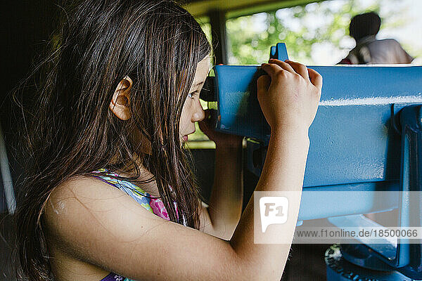 Side-view of a girl studying nature through large binoculars