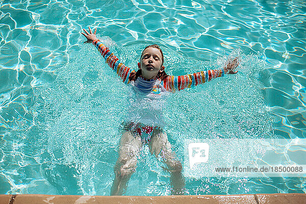 young girl swimming on back in pool on sunny day