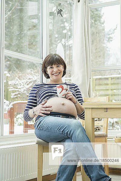 Portrait of pregnant woman sitting on chair with coffee mug