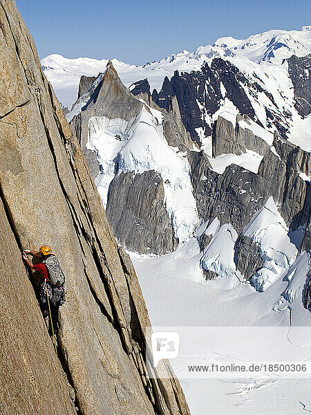 A climber ascends a crack in smooth granite on the north pillar of Cerro Fitz Roy  with Cerro Pollone  Cordon Marconi.