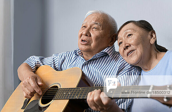 Senior man playing acoustic guitar and singing with his wife at home