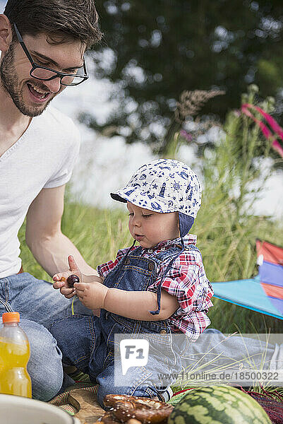 Father with his baby laughing and looking at a cherry on meadow in the countryside  Bavaria  Germany