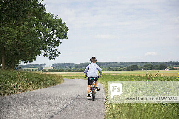 Rear view of a child riding bicycle on road in the countryside  Bavaria  Germany