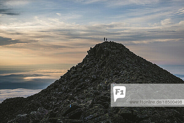two hikers stand on the summit of Katahdin  Maine at dawn. Silhouette.