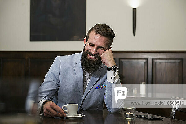 Well-dressed man looking at coffee cup and thinking while sitting at restaurant