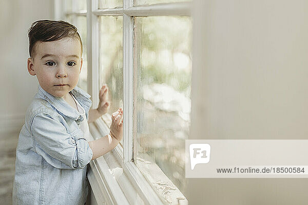 Toddler boy looking at camera by window in natural light studio
