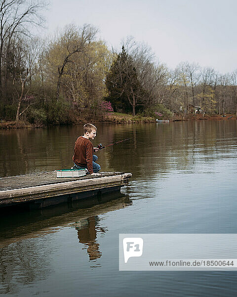 Child fishing off dock in lake during spring