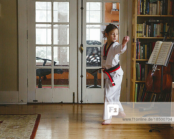 A young girl in uniform practices Taekwondo at home