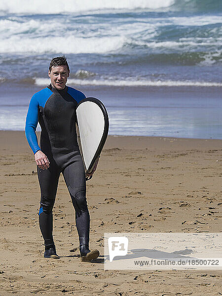 Young man carrying surfboard on Sopela Beach  Biscay  Basque Country  Spain