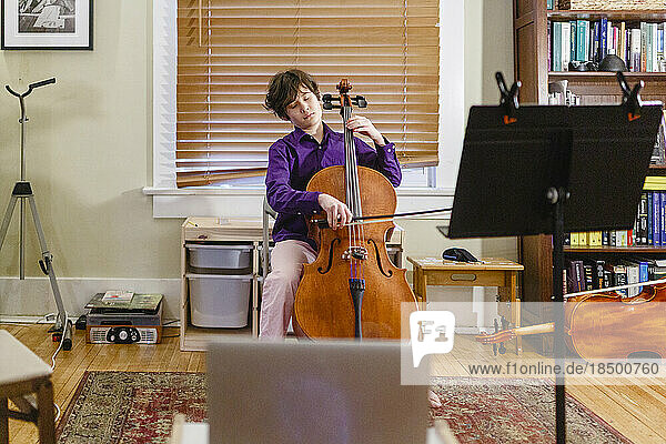 A young passionate boy plays cello in front of computer