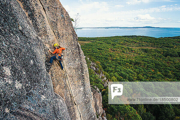 Woman rock climbing on vertical crack with ocean in background