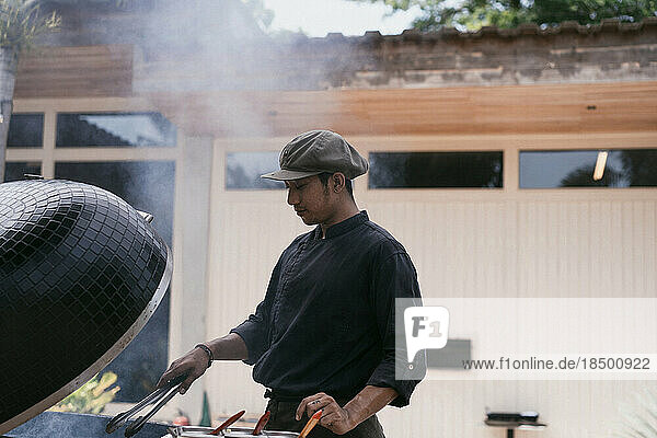 Asian man in uniform cooks on the grill outdoors. Kitchen staff