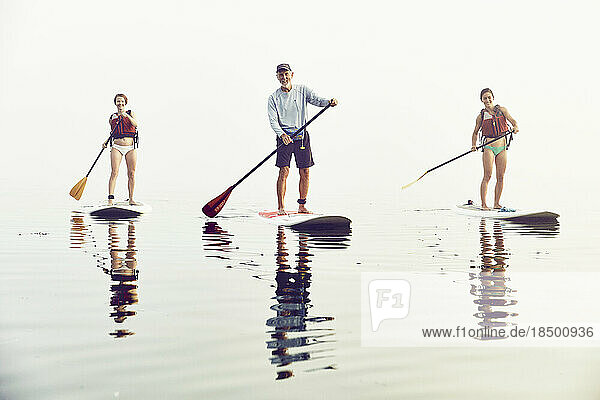 A group of friends standup paddle boarding on an early foggy morning