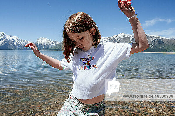Young girl dancing on lake shore near snowy mountains