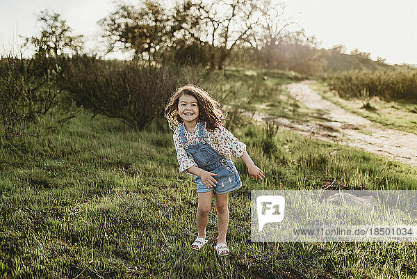 Full length view of young school-aged girl dancing in backlit field