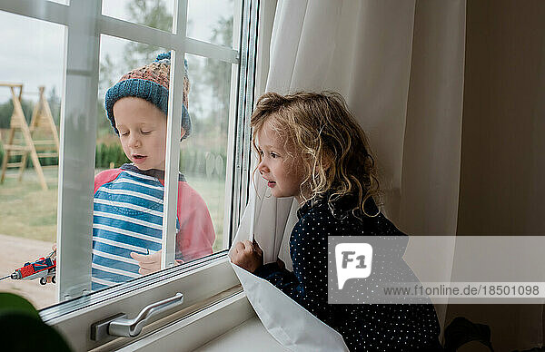 brother and sister looking through the window whilst playing