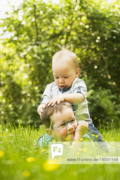 Small boy sitting on his brother in the garden