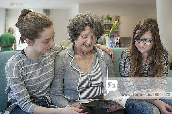 Girls reading magazine with senior woman in rest home