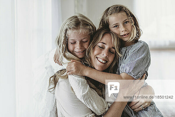 Daughters embracing smiling mother in natural light studio