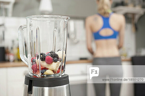 Mixer with fruits in the kitchen with young woman in the background  Bavaria  Germany