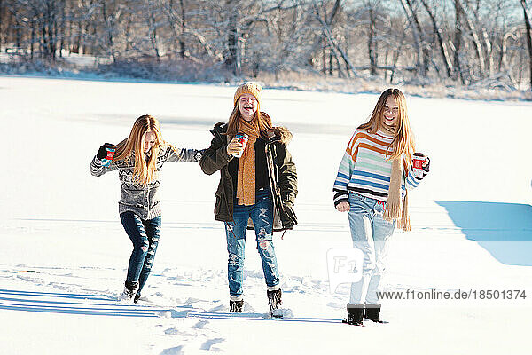 Three tween girls playing in the snow on a frozen lake on winter day.