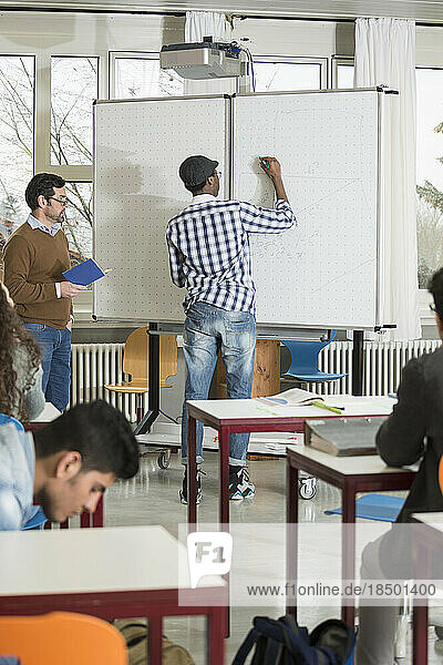 Student writing on whiteboard and teacher watching him School  Bavaria  Germany