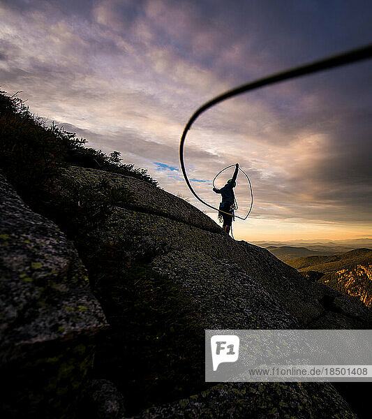 Woman coiling rock climbing rope at sunset on top of cliff