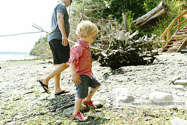Side view of a father and son walking on a rocky beach on a sunny day