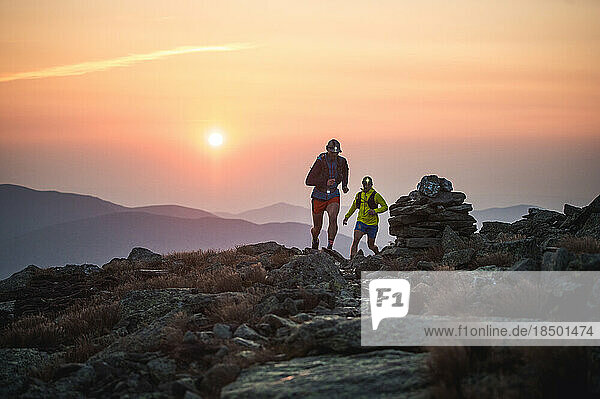 Silhouette of male trail runners running on rocky trail at sunrise