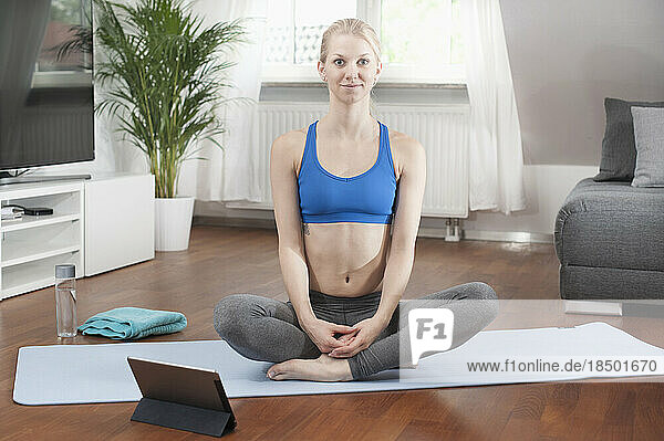 Young woman with digital tablet and doing yoga on exercise mat in living room  Bavaria  Germany