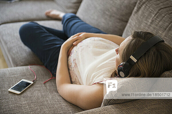 Pregnant woman lying on sofa and listening to music  Munich  Bavaria  Germany