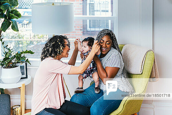 Cheerful mothers playing with cute baby boy in living room at home