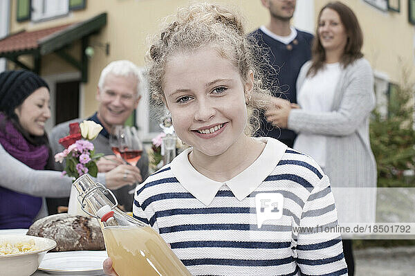 Portrait of a teenage girl holding apple juice and smiling with family in the background  Bavaria  Germany
