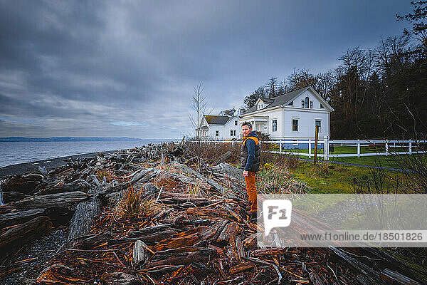 A man is standing on logs near Puget Sound and a historical building
