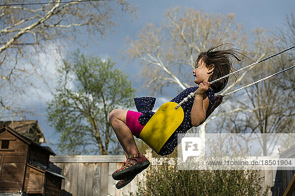 A happy girl on a yellow swing on a breezy  stormy spring day