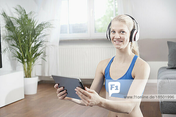 Portrait of a young woman using digital tablet and listening to music in living room  Bavaria  Germany