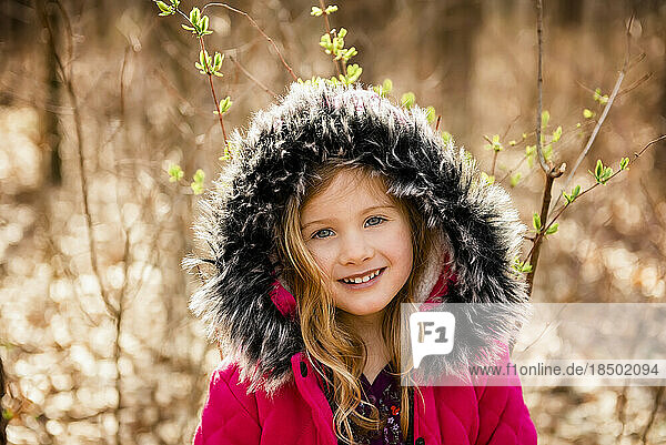 Smiling girl looks at camera with fur hood on head in Fall forest