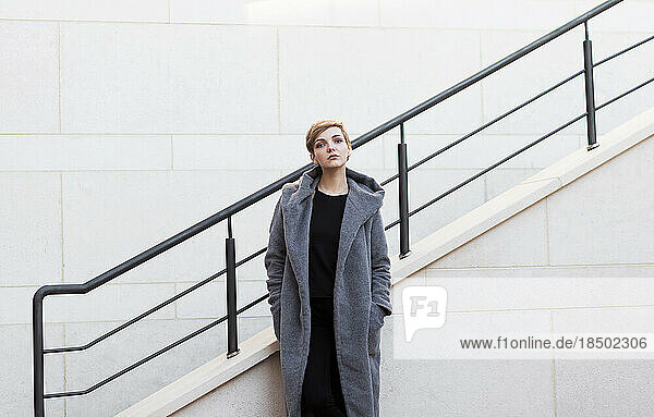 woman with short tousled hair in gray coat on stairs background