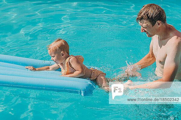 Dad and baby daughter swim on an inflatable mattress in the outd