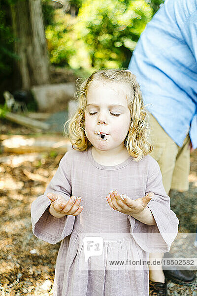 Straight on view of a young girl eating a s'more marshmallow sandwich